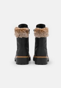 Botas de tobillo de cuero negro con un acogedor puño de piel sintética marrón, suelas de goma y una cremallera decorativa en el lateral. Detalles de costura a lo largo de la suela.