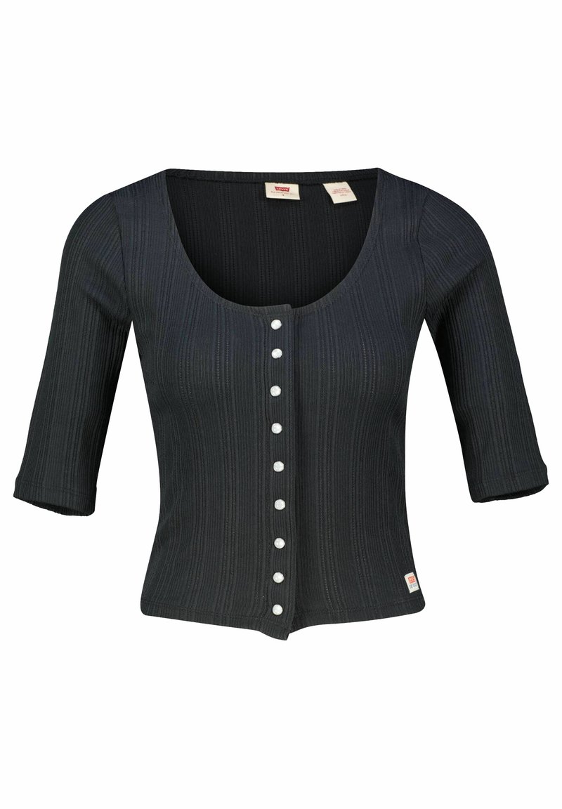 Musta ribattava neulepaita, jossa on pyöreä pääntie, kolmanneksen pituiset hihat ja nappikiinnitys valkoisilla takeilla. Pienen logotagin sijaitsee helmassa.