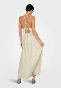 Robe maxi bleu clair à fleurs avec un décolleté dans le dos, des bretelles croisées ajustables et un tissu fluide et texturé. Sandales à talons bleues.