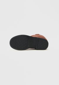 Zapato de cuero marrón con punta redonda, parte superior texturizada y suela de goma negra con un patrón de diamante para mayor tracción.