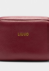 Bordo spalvos odinė stačiakampė kuprinė su tekstūruotu paviršiumi. Priekinėje pusėje yra auksinis „LIU•JO“ logotipas. Plokščias dizainas su švariais kraštais.