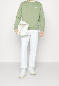 Sudadera verde claro con logo blanco de Nike, combinada con pantalones blancos y zapatillas blancas. Lleva un bolso beige claro.