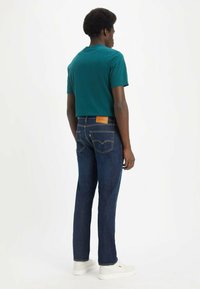 Maglietta a maniche corte teal abbinata a jeans in denim blu scuro con un'etichetta in pelle e cuciture a contrasto. Sneakers bianche completano il look.