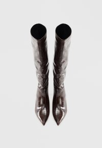 Par de botas altas de cuero marrón oscuro con textura de cocodrilo y punteras puntiagudas, de pie sobre un fondo claro liso.
