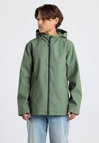 Green waterproof jacket with a front zipper, hood, and side pockets; smooth texture and relaxed fit; paired with light blue jeans.
