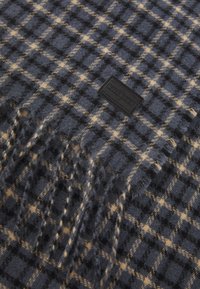 Plaid scarf in navy and tan, crafted from soft fabric, featuring fringed edges and a textured weave, with a black label accent.