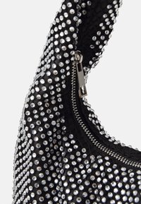 Sac à main noir couvert de strass avec une surface texturée, doté d'une fermeture éclair et d'une poignée courbée.