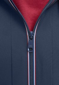 Marinejacke mit einem Frontreißverschluss und rot-weißen gestreiften Akzenten am Kragen. Der Stoff hat eine glatte Textur.