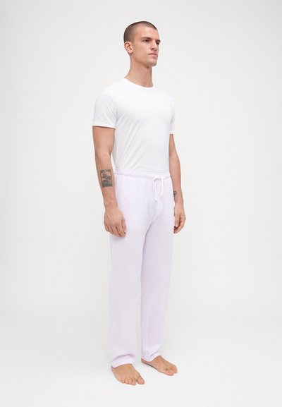 Camiseta blanca de algodón combinada con pantalones de tiro morado claro con cordón. Los pantalones tienen un corte relajado y bolsillos laterales, con una textura suave.