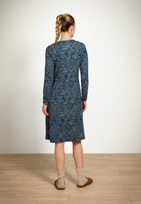 Langärmliges Kleid in Dunkelblau mit floralem Muster, knielang, aus weichem Stoff. Kombiniert mit beigen Socken und braunen Hausschuhen.