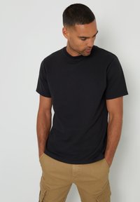 Schwarzes Rundhals-T-Shirt aus Baumwolle, mit kurzen Ärmeln und lockerem Schnitt, getragen mit khakifarbenen Cargo-Shorts. Einfaches, klassisches Design.