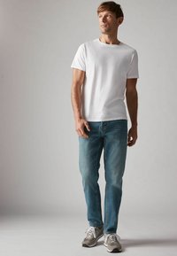 Camiseta blanca de cuello redondo, jeans azul claro y zapatillas grises. Los jeans tienen un corte recto y un ligero desgaste; las zapatillas tienen cordones blancos.