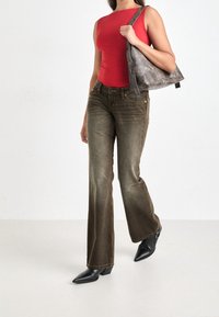 Rød ærmeløs top, olivengrønne flared jeans, sorte spidse ankelstøvler og en grå skuldertaske med en glat tekstur.