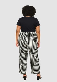 Top nero a maniche corte abbinato a pantaloni a gamba larga con un audace motivo geometrico bianco e nero. I pantaloni hanno una vestibilità ampia e una cintura elastica.