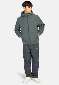 Ljust grått huvtröja med en hel dragkedja, kombinerad med mörka rutiga byxor och vita sneakers, med en avslappnad passform och elastiska ärmslut.