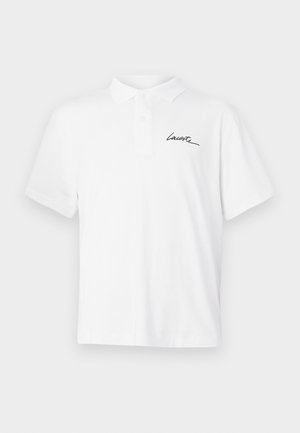 Polo blanc à manches courtes avec col et boutons, avec « Lacoste » en écriture noire sur le côté gauche de la poitrine.