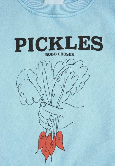 Camicia azzurro chiaro con testo nero "PICKLES BOBO CHOSES" sopra una mano disegnata a mano che tiene delle verdure a foglia con radici rosse.