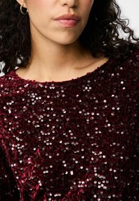 Bordo blizgučiais padengtas viršus su apvaliomis iškirpėmis ir minkšta, tekstūruota medžiaga, su atspindinčiais blizgučiais, siuviniais visame paviršiuje, suteikiančiais papildomą žvilgesį.