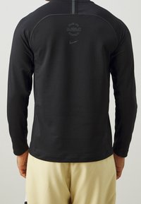 Schwarzes, langärmliges Sportshirt aus glattem, leichtem Material. Verfügt über ein Logo und Text am oberen Rücken, mit flachen Nähten und einer taillierten Passform.