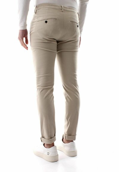 Chinos beige con una vestibilità slim, due tasche posteriori e orli arrotolati, abbinati a sneakers bianche, che mostrano una texture del tessuto liscia.