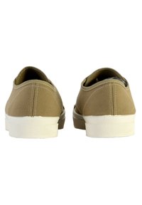 Zapatillas de lona beige sin cordones con una suela de goma blanca y detalles texturizados. Parte trasera redondeada con costuras decorativas. Diseño casual para el uso diario.