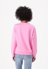 Sweatshirt rose à manches longues, avec des bords côtelés aux poignets et en bas, et un col rond. Porté avec un jean déchiré bleu clair. Texture de tissu lisse.