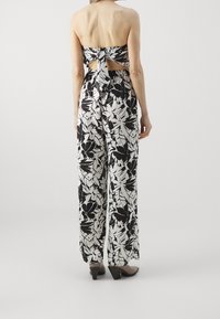 Mono de flores en blanco y negro con un top sin mangas, atado en la parte posterior, que presenta piernas anchas y un ajuste relajado. Se ven un par de zapatos de tacón.