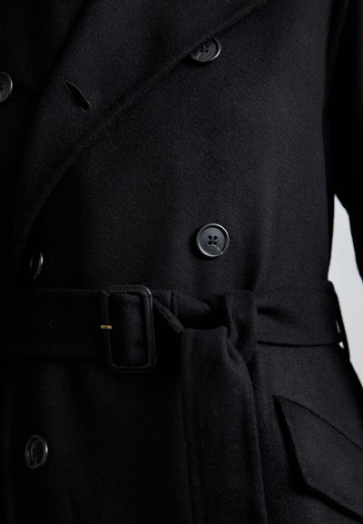 Μαύρο παλτό από μείγμα μαλλιού με διπλή κουμπωτή μπροστά, μεγάλους κόμπους, ζώνη στη μέση και πλαϊνές τσέπες. Υφασμάτινη επιφάνεια με απαλή υφή.
