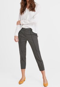 Bílá halenka s dlouhým rukávem v kombinaci s černobílými kalhotami s puntíky, střih slim fit a zkrácená délka. Žluté ploché boty dokončují celkový vzhled.