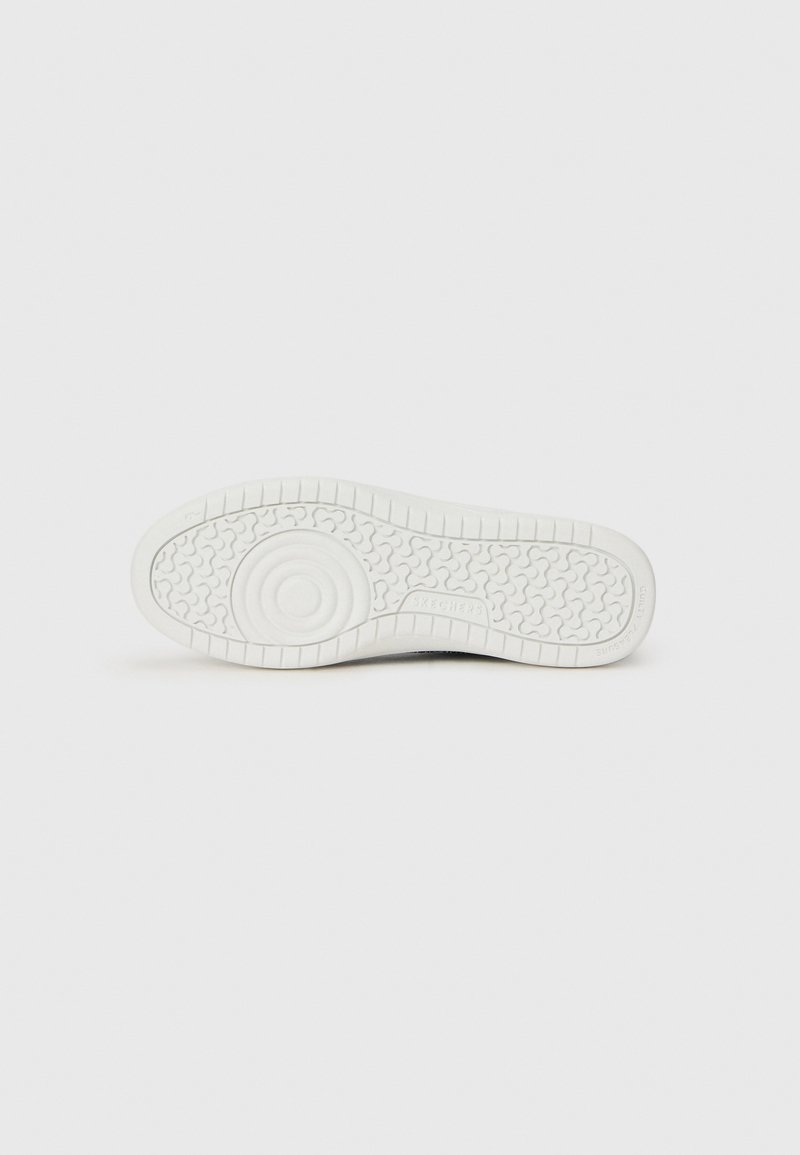 Le dessous d'une sneaker blanche présente une semelle texturée avec des motifs circulaires et ondulés, étiquetée "SKECHERS."
