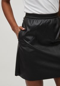 Zwarte leren rok met een hoge tailleband, voorzien van een gladde textuur en zijzakken; snit die boven de knie valt.