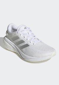 Witte sportieve schoen met mesh bovenzijde, drie grijze strepen, ronde vorm, getextureerde zool en reflecterende accenten. Minimalistisch ontwerp.