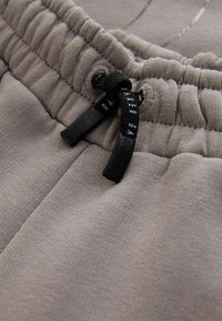 Grå joggingbukser med en elastisk talje og sort snor. Stoffet virker blødt med en glat tekstur og diskrete syningsdetaljer.