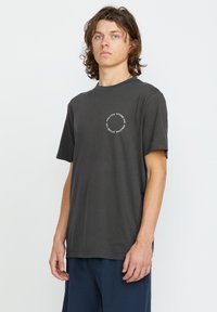 T-shirt noir à manches courtes en coton, avec un imprimé graphique circulaire blanc sur la poitrine. Coupe décontractée et col rond.