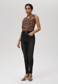Blusa sin mangas de estampado de leopardo combinada con jeans skinny negros de cintura alta y tacones negros con tiras, con detalles de botones de metal.