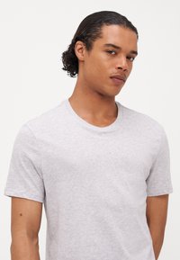 T-shirt en coton gris avec un col rond et des manches courtes, présentant une texture lisse et une coupe décontractée. Pas de logo ou de motifs visibles.