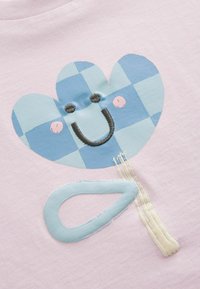 Camiseta rosa con un gran diseño de flor a cuadros azules y blancos, una cara sonriente y un tallo texturizado azul claro con acentos beiges.