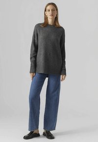 Maglione grigio a maglia con scollo tondo, abbinato a jeans blu a vita alta. Dettagli includono polsini a coste e mocassini in pelle.