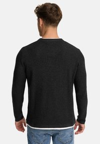 Suéter negro de punto con un acabado texturizado y un cuello redondo, llevado sobre una camisa blanca, combinado con jeans de mezclilla azul claro.