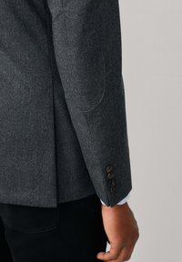 Grau Wolle Blazer mit taillierter Passform, Ellbogen-Patches und vier dunklen Knöpfen an den Ärmelbündchen. Glatte Textur mit strukturiertem Design.