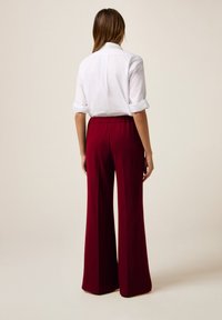 Burgundy byxor med vida ben, gjorda av en slät textil, med resår i midjan och en lång silhuett, i kombination med en krispig vit skjorta med uppvikt ärm.