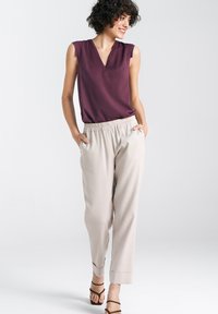 Beżowe spodnie z elastycznym paskiem, zestawione z bezrękawnikiem w kolorze burgundowym i dekoltem w serek. Stylizacja ma luźny krój i gładką fakturę.