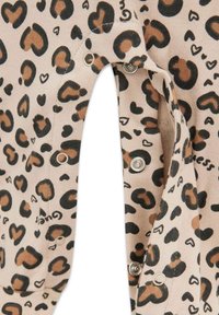 Tan stof met een leopardprint in zwart en bruin, met hartvormen. Drukknopen zichtbaar aan de zijkant. Zachte textuur.