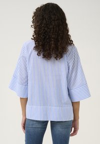 Dryžuota medvilninė bluzonė su išsiplėtusiais rankovėmis, turinti keičiantis šviesiai mėlynos ir baltos spalvos dryžius. Nugarinė dalis yra šiek tiek ilgesnė nei priekinė.