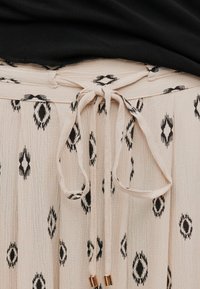 Μπεζ φούστα με μαύρα γεωμετρικά σχέδια δεμένη στη μέση με υφασμάτινη ζώνη σε φιόγκο, σε συνδυασμό με μαύρο τοπ.