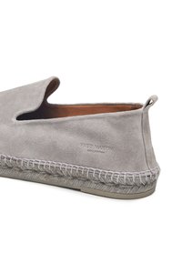 Grauer Slip-On-Schuh aus Wildleder mit strukturierter Oberfläche, einem gewebten Besatz und einem markenbezogenen Detail an der Seite. Flache Gummisohle.