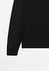 Sort strikket sweater med langeærmer, der har ribbede manchetter og kant. Glat tekstur og klassisk design, velegnet til afslappet brug.