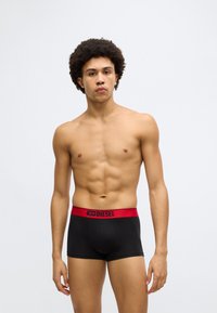 Boxeri negri cu talie elastică roșie, pe care este inscripționat cuvântul „DIESEL” într-un mod proeminent. Țesătura pare netedă și strâmtă.