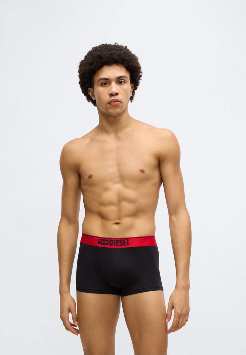 Boxeri negri cu talie elastică roșie, pe care este inscripționat cuvântul „DIESEL” într-un mod proeminent. Țesătura pare netedă și strâmtă.