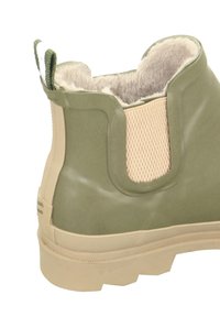 Grüner Gummistiefel mit einem tanfarbenen Netzpanel, plüschigem grauen Futter und abgerundetem Absatz. Verfügt über eine Zuglasche an der Rückseite für ein einfaches Anziehen.